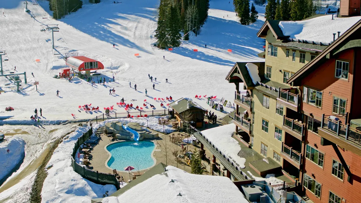 An exterior view featuring snow-covered ski slopes alive with skiers and snowboarders, a sparkling swimming pool, and the inviting architecture of the lodge. The scene is energetic and captures both winter sports activity and spaces for relaxation, with families and friends enjoying the outdoors.