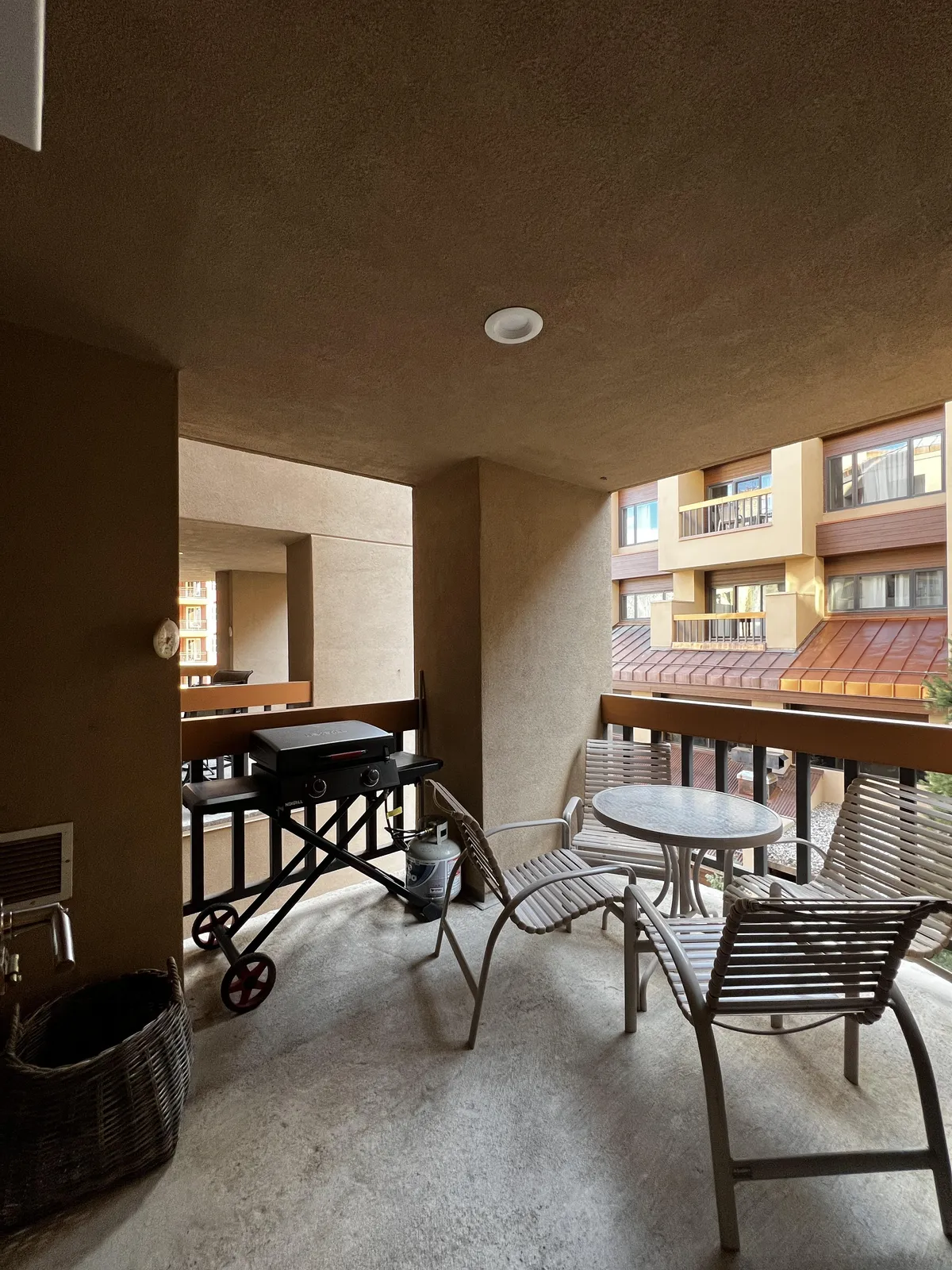 This image shows a private balcony with a propane grill, outdoor dining table, and comfortable chairs. The balcony is enclosed by a railing, offering a vantage point to enjoy views beyond. The setting is inviting, with plenty of space to socialize, dine, or unwind while surrounded by mountain air.