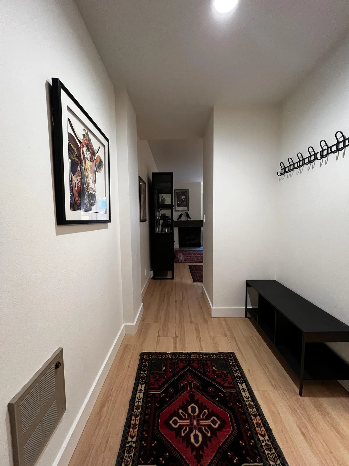 The image showcases the stylish entryway of the studio, featuring elegant black furniture, a vibrant decorative rug, and eye-catching local artwork on the wall. The space radiates warmth and charm, setting a welcoming tone for guests as they arrive.