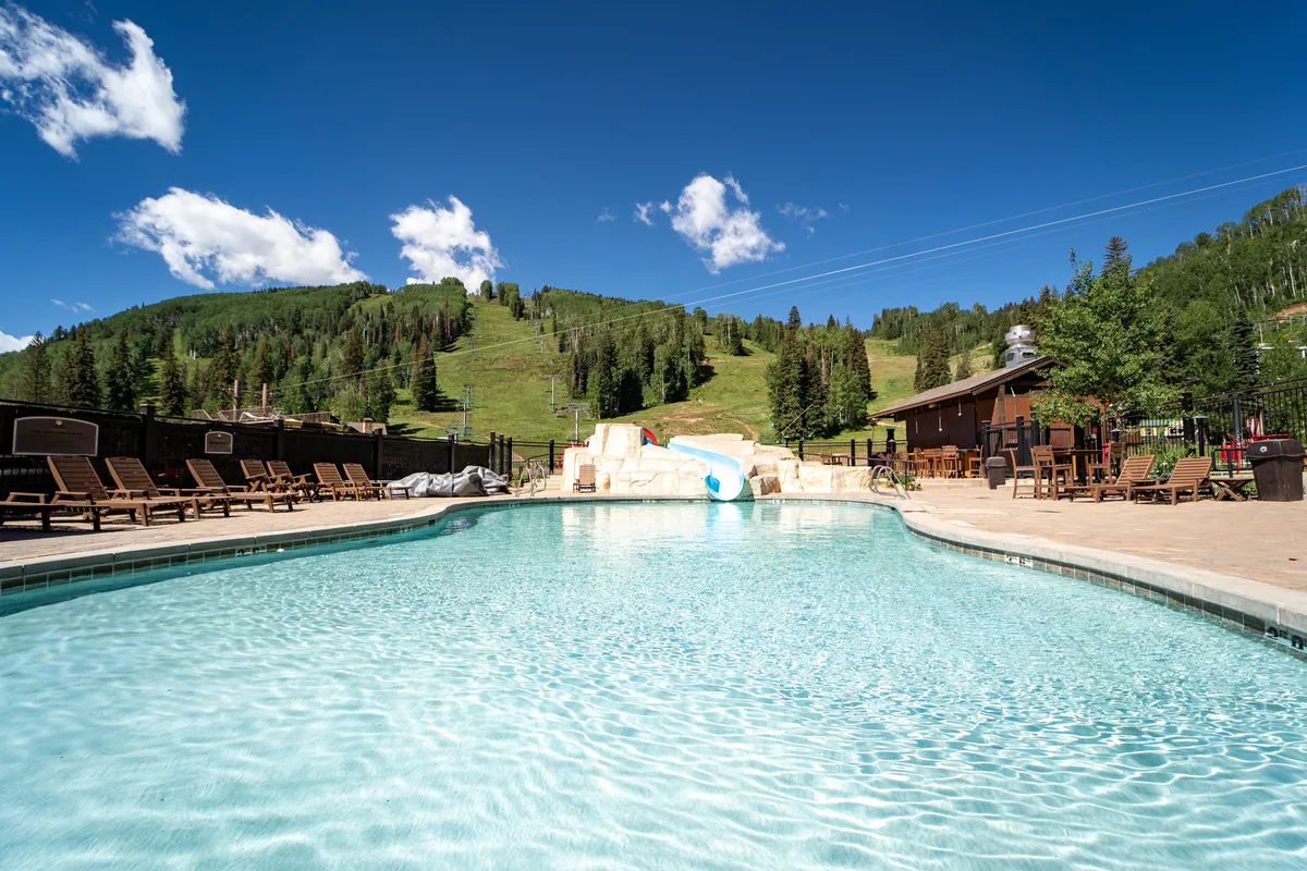 This exterior photo features a sparkling swimming pool with lounge chairs and a poolside bar, all set against a mountain backdrop. The atmosphere is relaxed, with hints of social interaction and leisure, suggesting both community and tranquility.